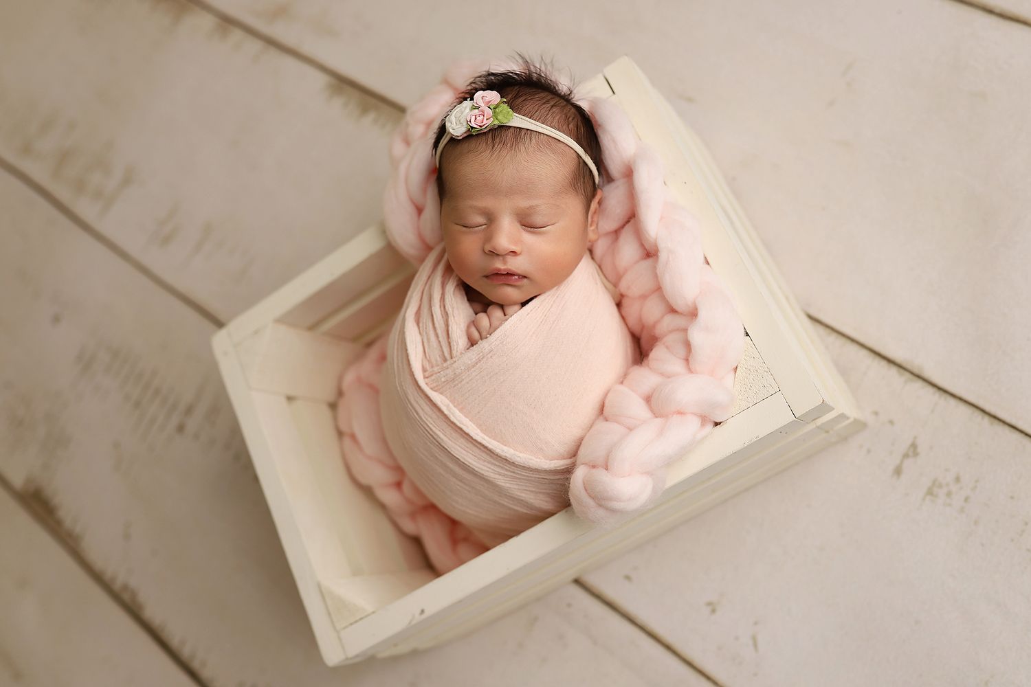 Newborn baby sleeping peacefully on soft white blanket with delicate pink headband in studio setting.