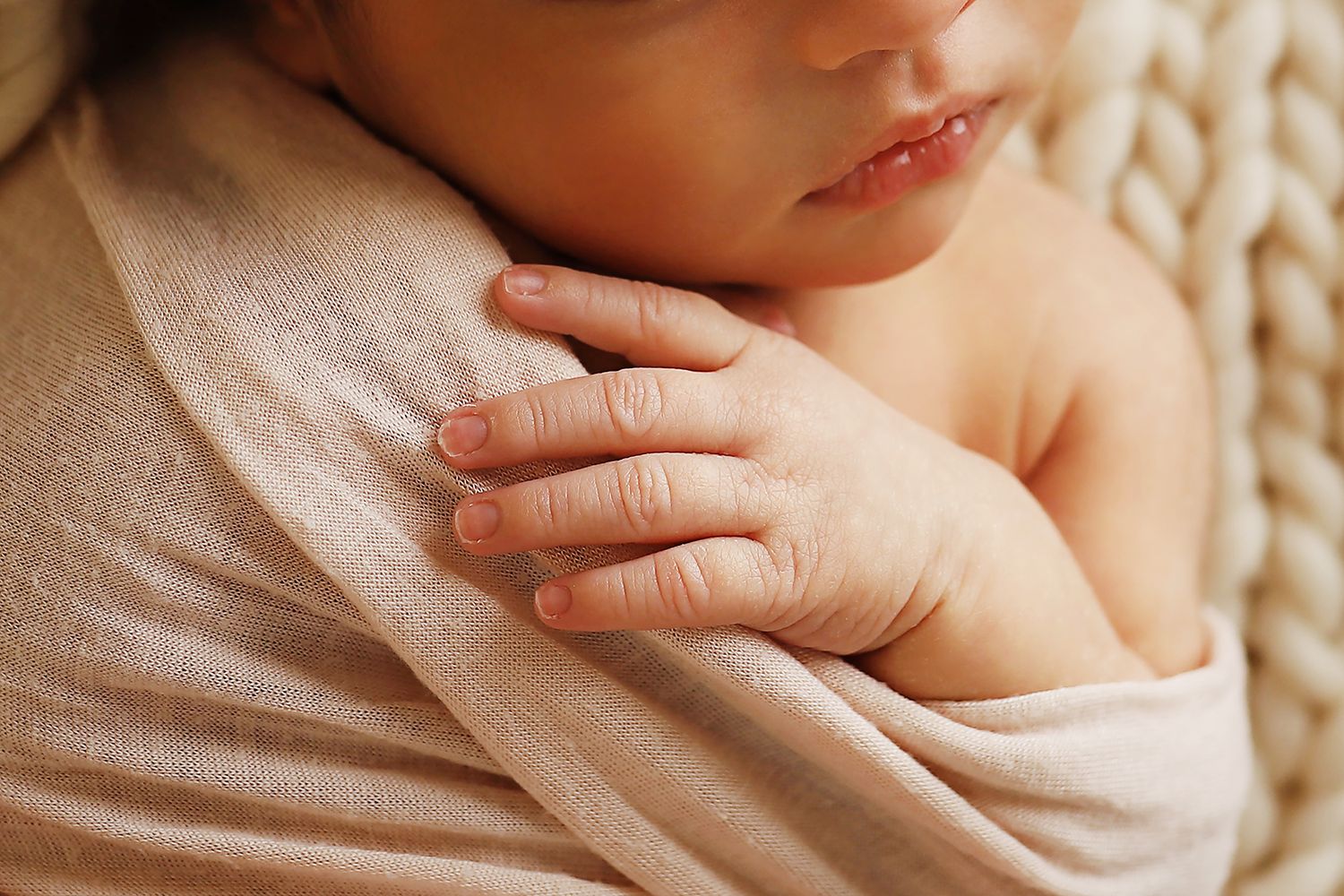 Close-up view of gentle hands tenderly holding a small baby in soft natural light.