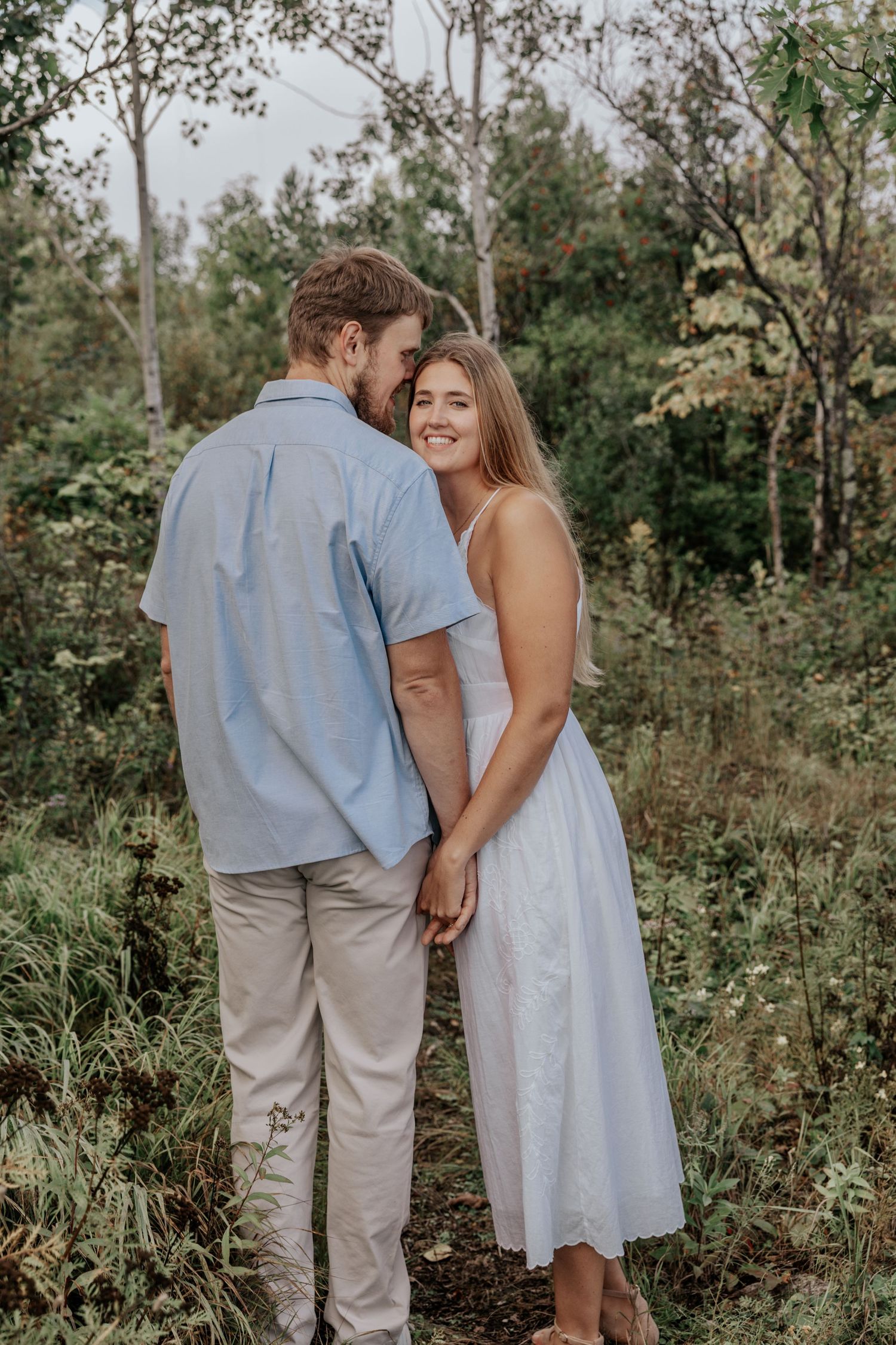 A couple shares an intimate moment in a natural outdoor setting wearing light blue and white clothing.