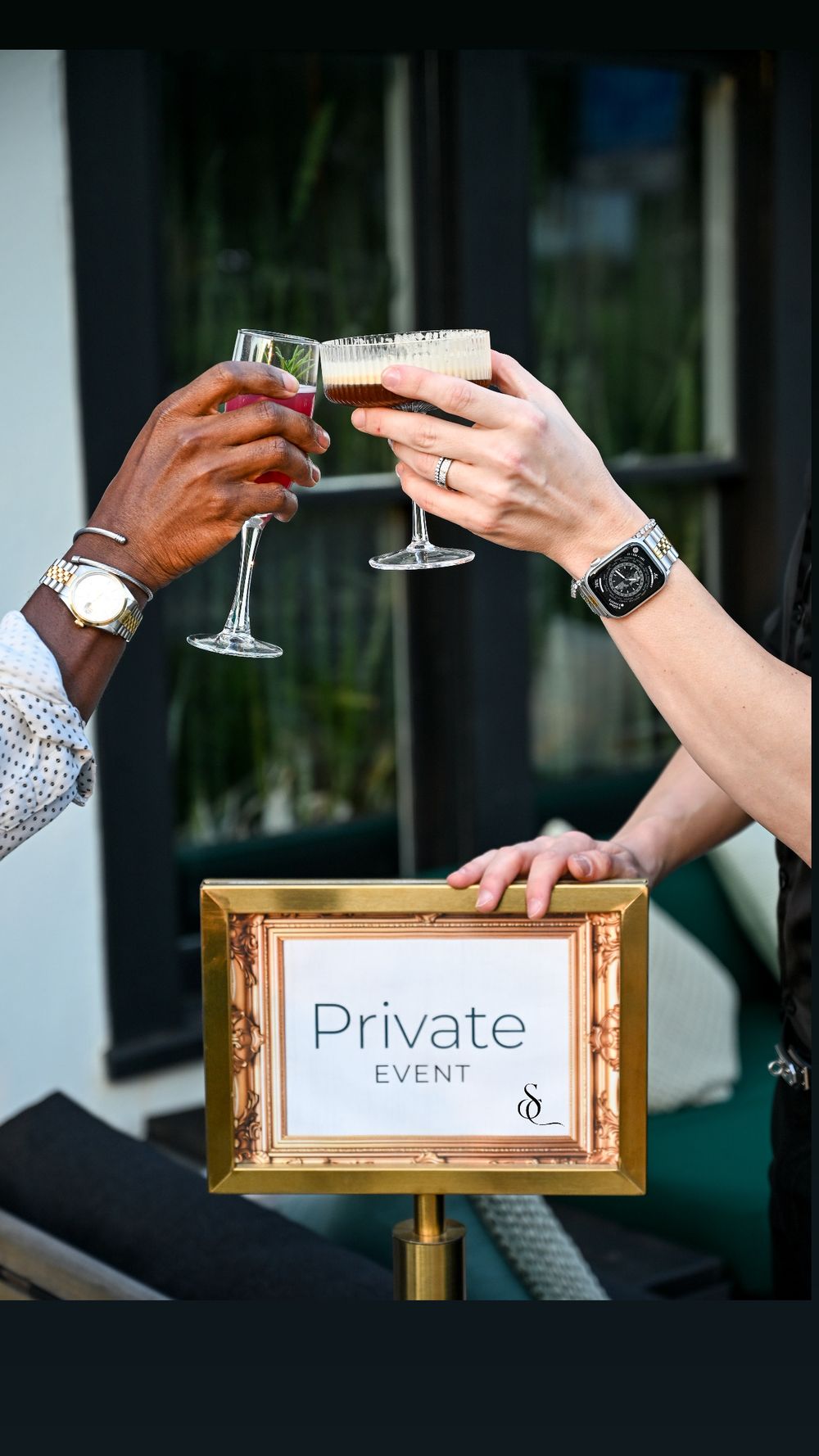 Champagne glasses clink together at a private event with ornate gold signage frames in the background.