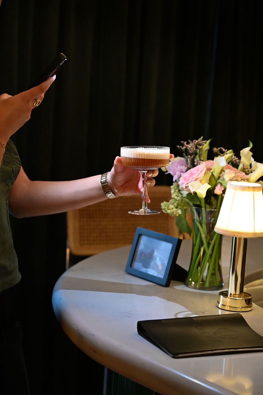 A dimly lit restaurant scene showing hands gesturing near an illuminated tablet display on a white table.