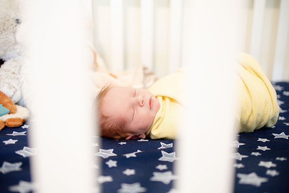 Swaddled newborn baby sleeping in white crib with navy star-print sheets.
