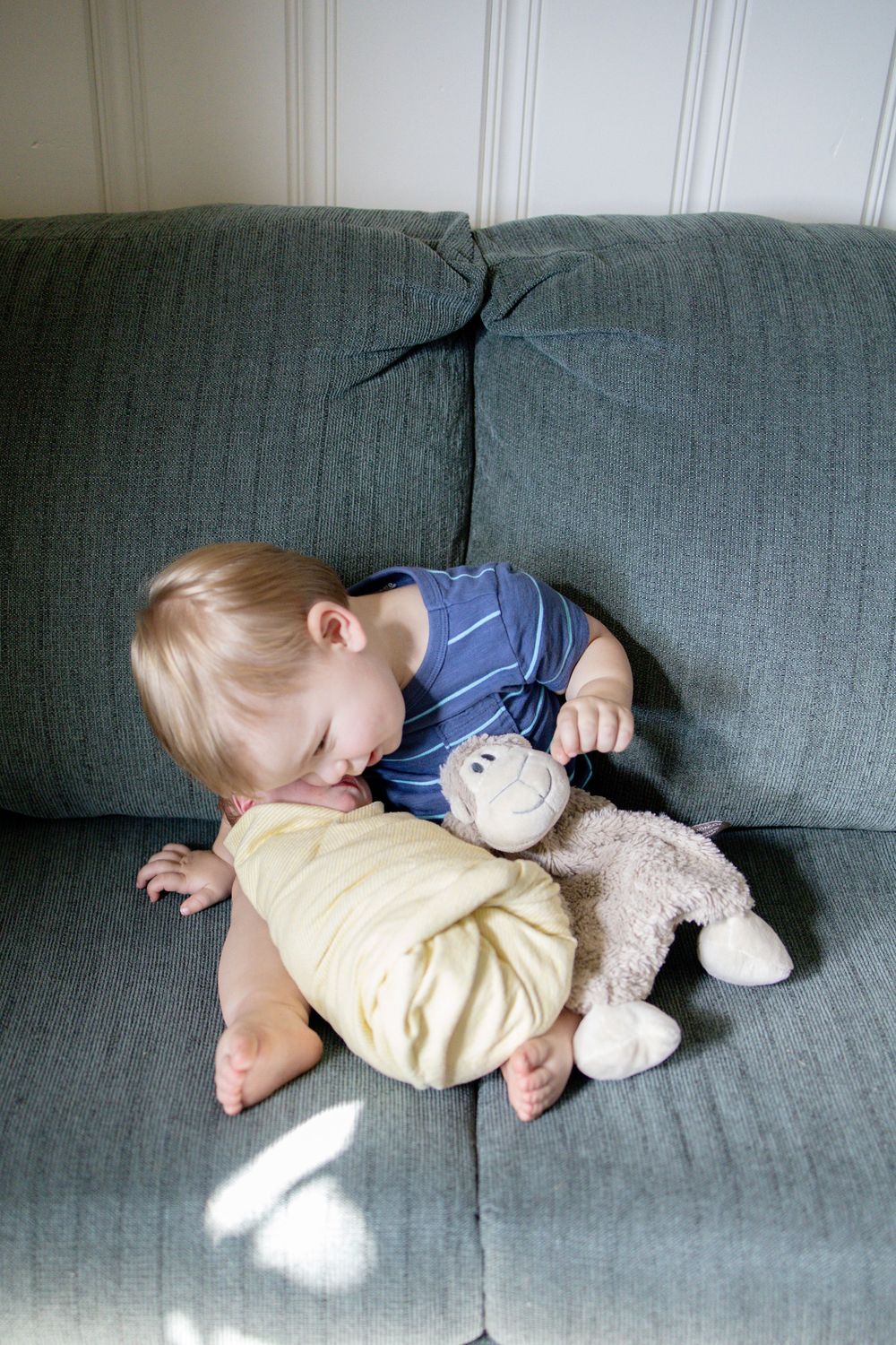 Toddler boy in blue shirt playing with stuffed monkey toy on gray sofa.