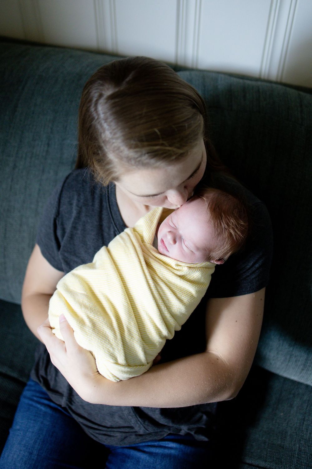 Mother tenderly kissing her swaddled newborn baby wrapped in yellow blanket.