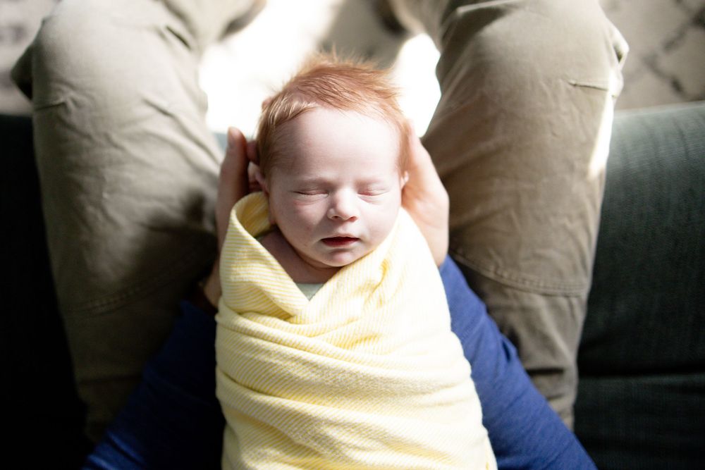Newborn baby swaddled in yellow blanket sleeping peacefully in parent's hands.