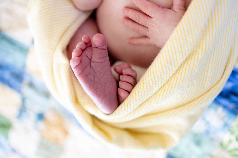 Close-up of a newborn babys tiny feet peeking out from a soft yellow swaddle blanket.