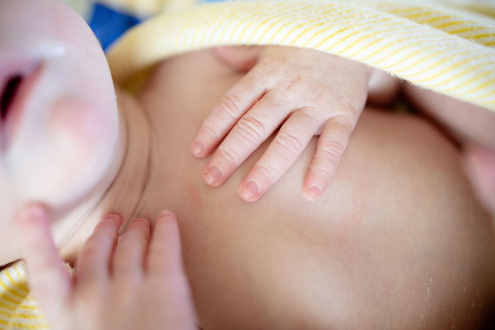 Close-up of newborn baby's tiny hands resting on chest wrapped in yellow swaddle.