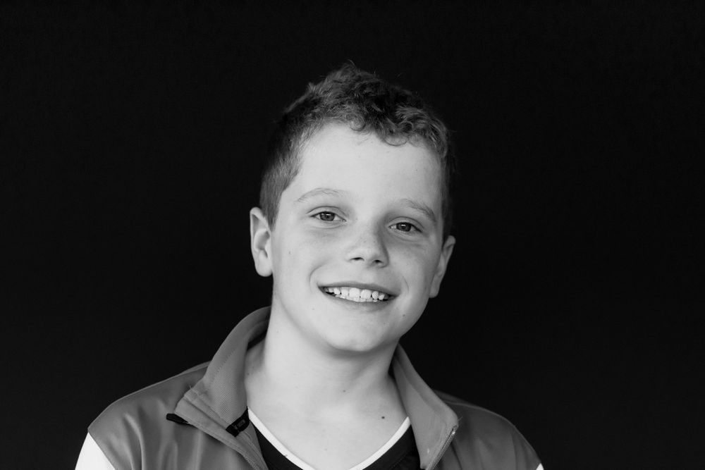 Smiling preteen boy with short hair wearing a jacket in a black and white portrait photo.