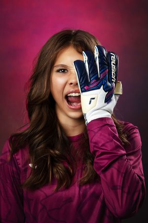 Soccer player in burgundy jersey wearing goalkeeper gloves poses against dark background.