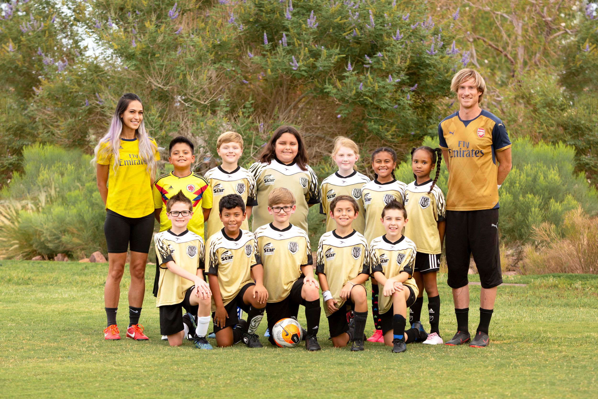 Soccer team sitting in row on grass field wearing matching yellow uniforms.
