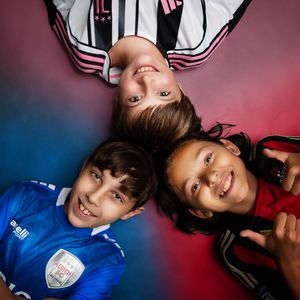 Youth soccer players lying down wearing different colored jerseys against colorful background.