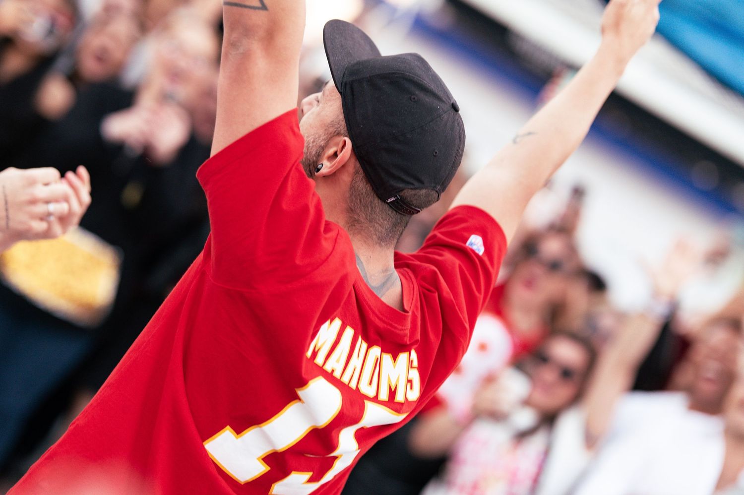 Fan in red jersey raises arms in celebration during an exciting sports moment.