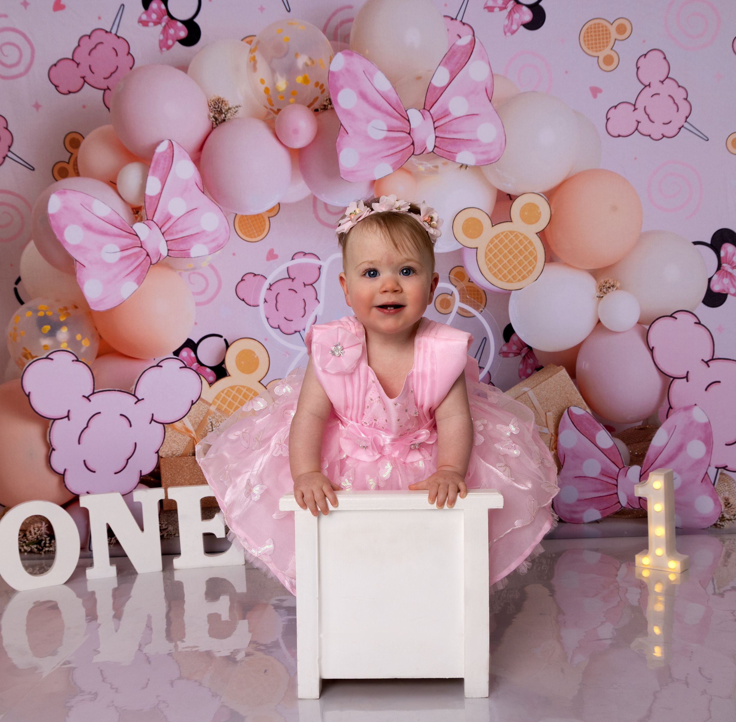 Pink balloon and floral backdrop with 'ONE' text display creates a whimsical first birthday party setting.