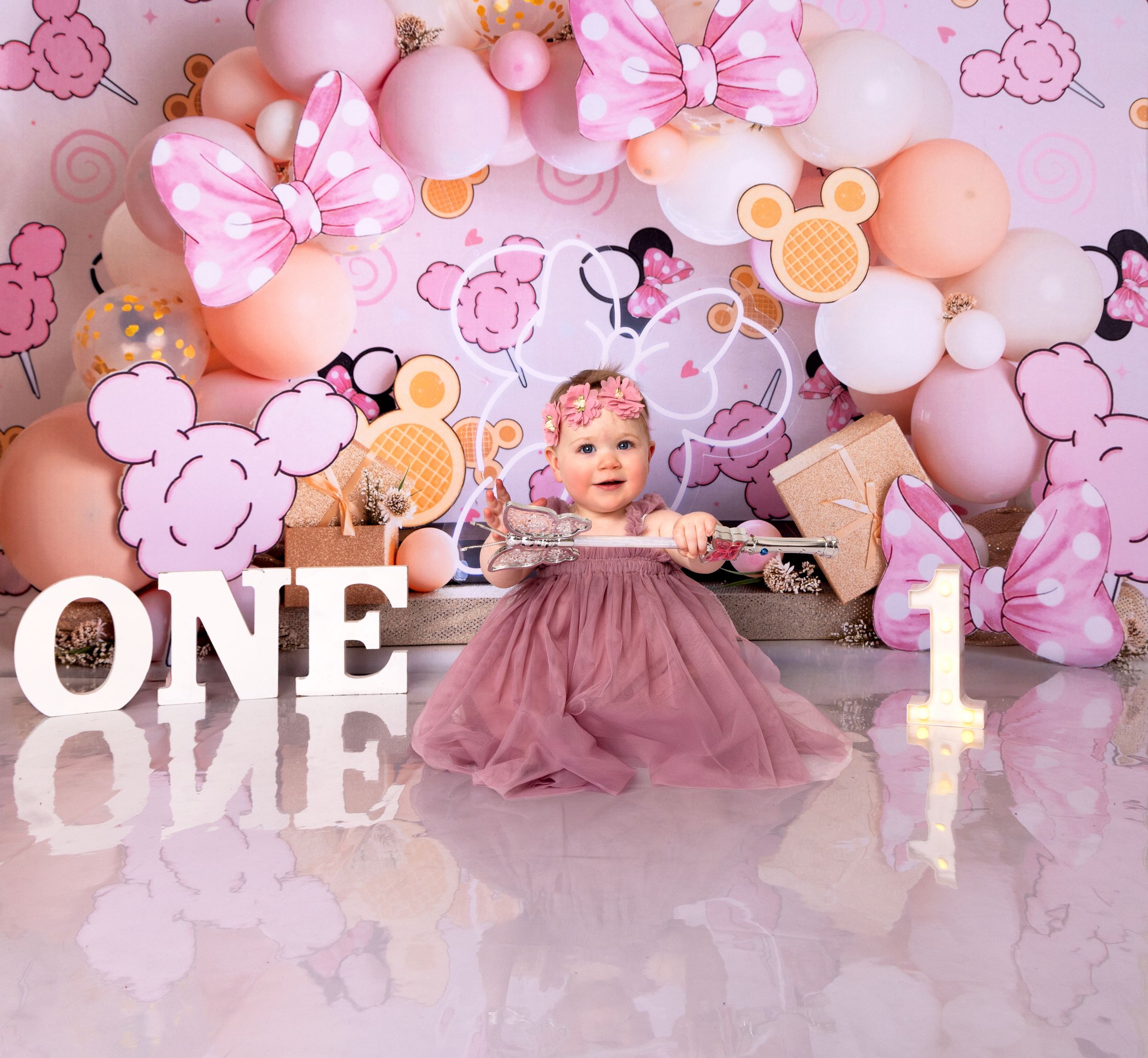 Pink and peach balloon arch with decorative elements creates a soft, romantic backdrop for a first birthday celebration.