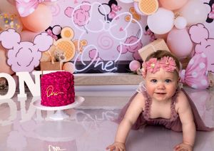 Baby sitting on floor surrounded by pink balloons and decorative elements in a professional photo setup.