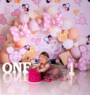 First birthday cake smash photo session with pink and peach balloon decorations against floral backdrop.