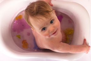 Baby in pink tub surrounded by pink bath petals and bubbles.