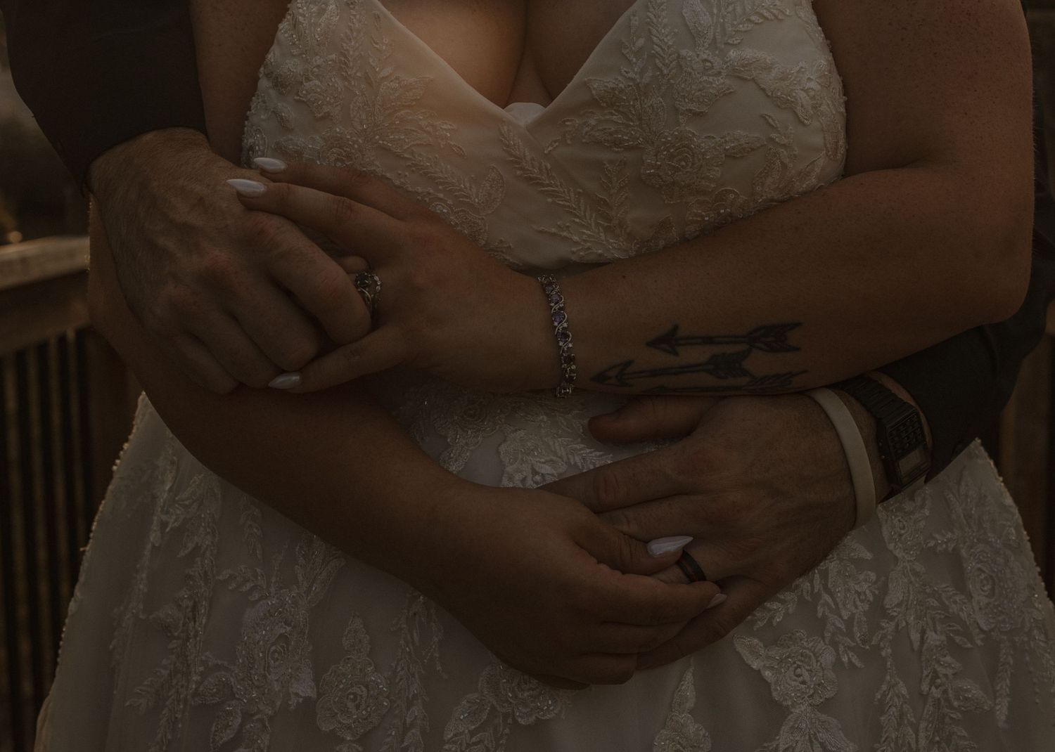 Close-up details of hands holding and touching a white lace wedding dress in romantic lighting.