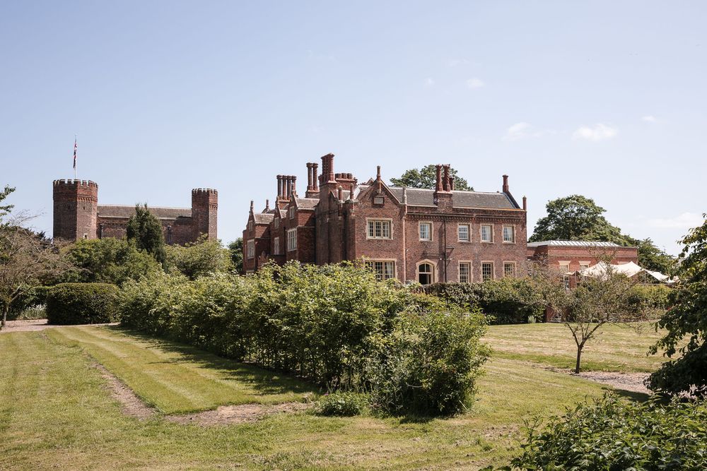 Historic brick manor buildings and grounds viewed across a sweeping green landscape.