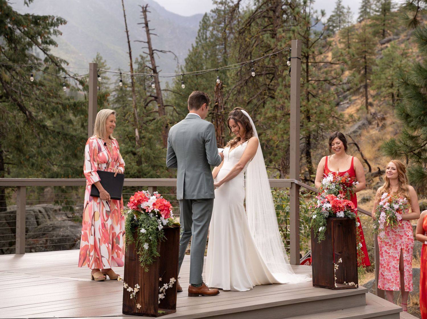 An outdoor mountain wedding ceremony with floral decorations and pine trees in the background.