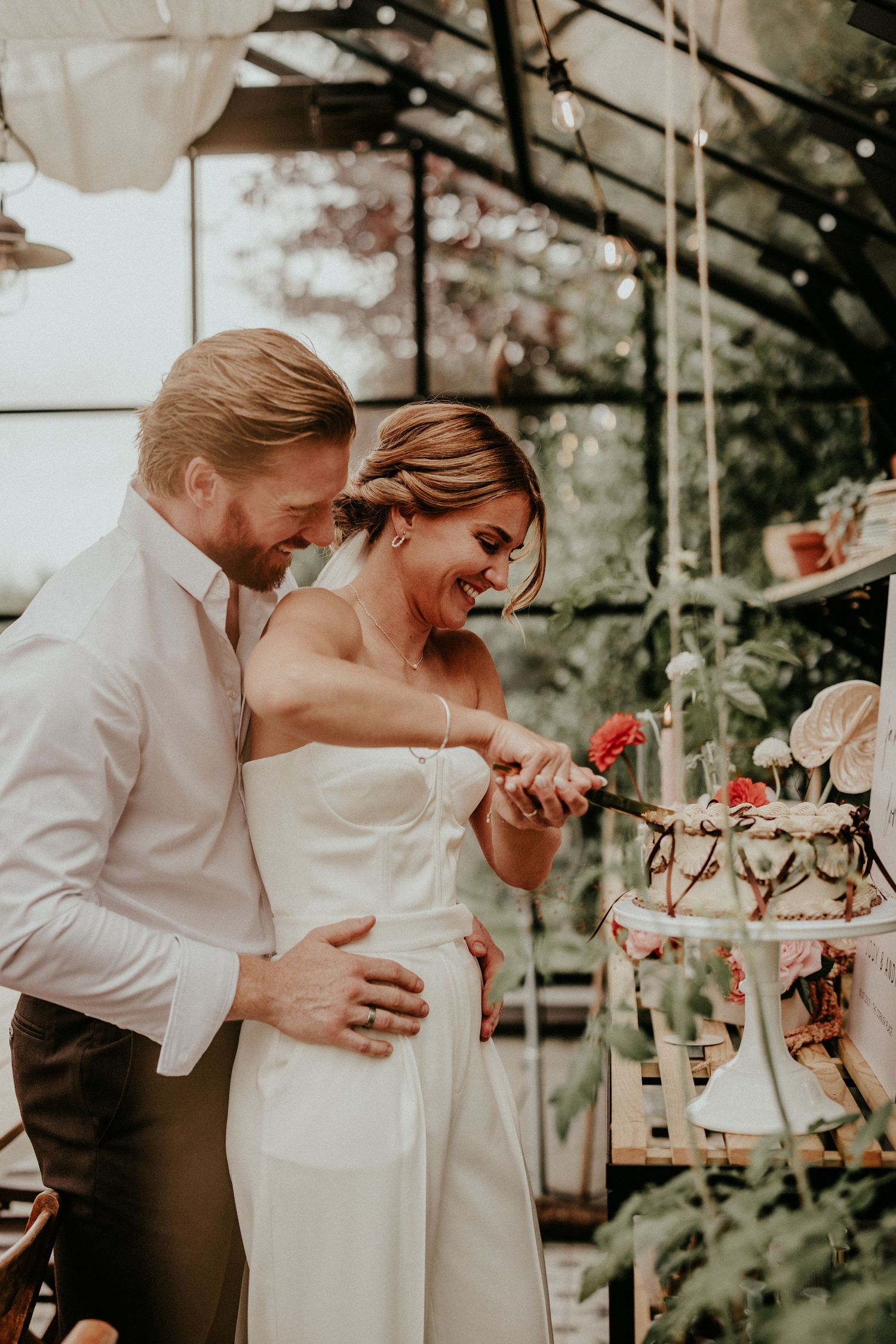 Couple shares joyful laughter while sitting at an elegant table setting with floral decor at outdoor garden event.