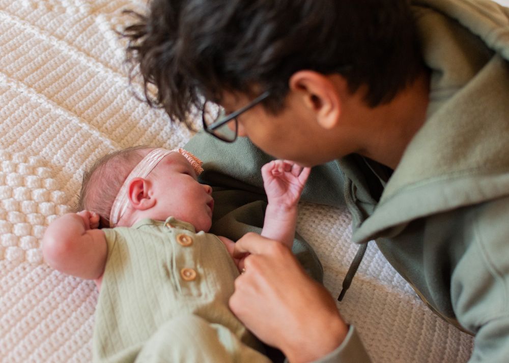 older brother looking down lovingly at newborn sister on bed