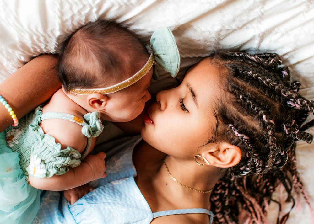 older sister holding newborn sister on bed lying down