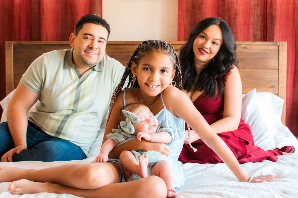 family with mom, dad, daughter holding newborn daughter on bed