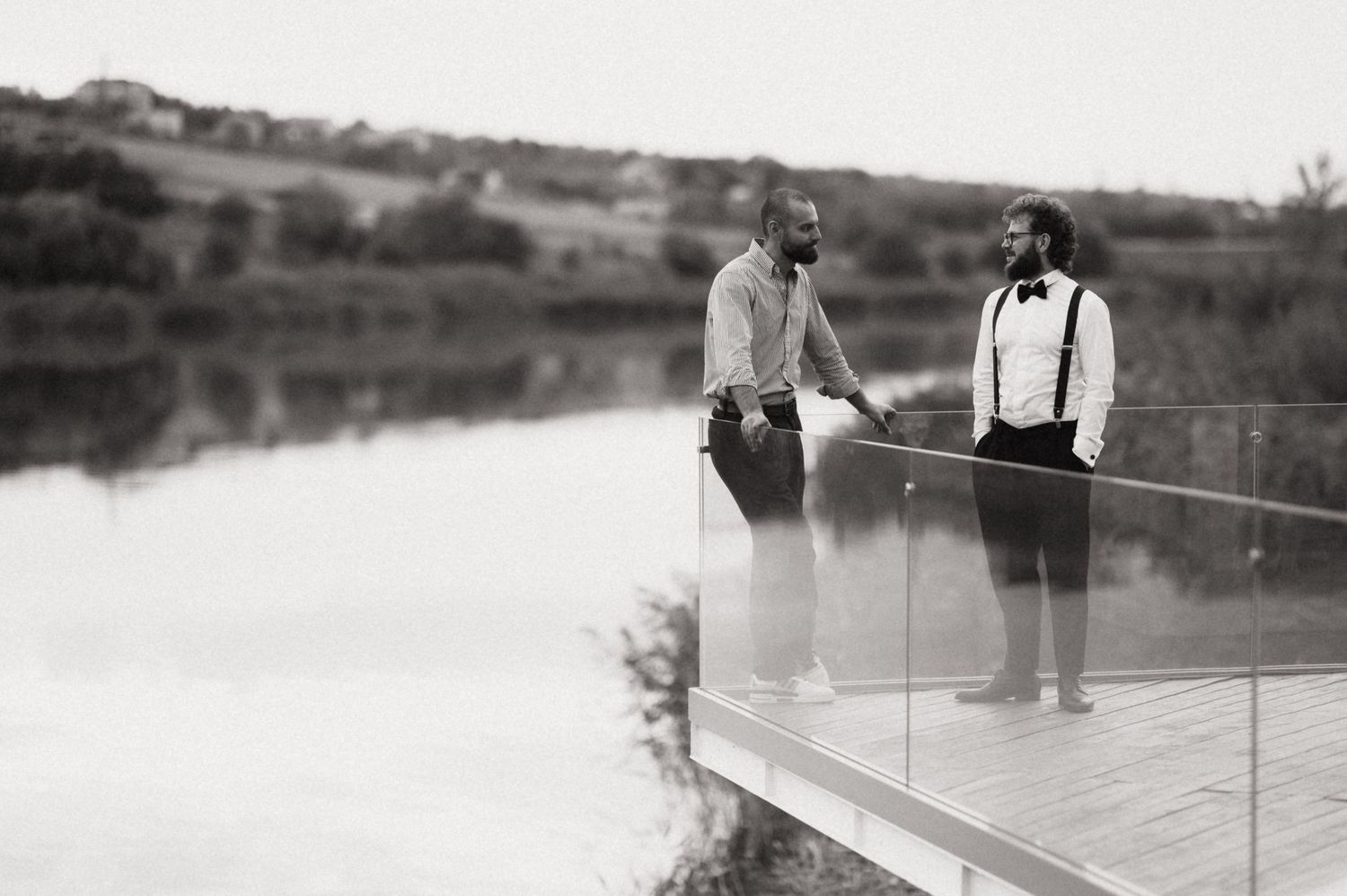 A group of people stand on a wooden dock overlooking a calm lake or pond in a black and white vintage photograph.