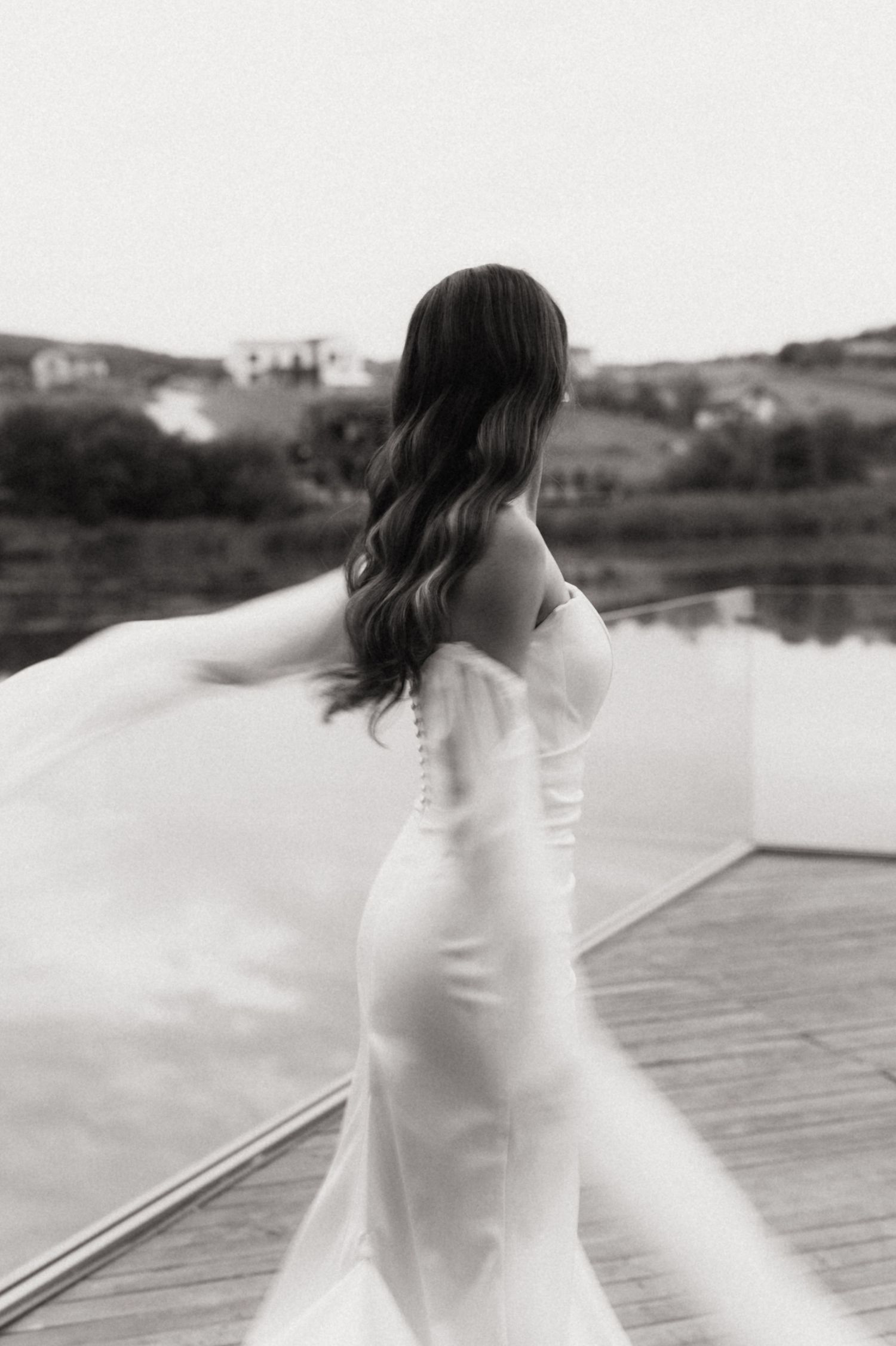 A person in a white dress stands on a wooden dock by a serene lake in a series of artistic black and white photos.