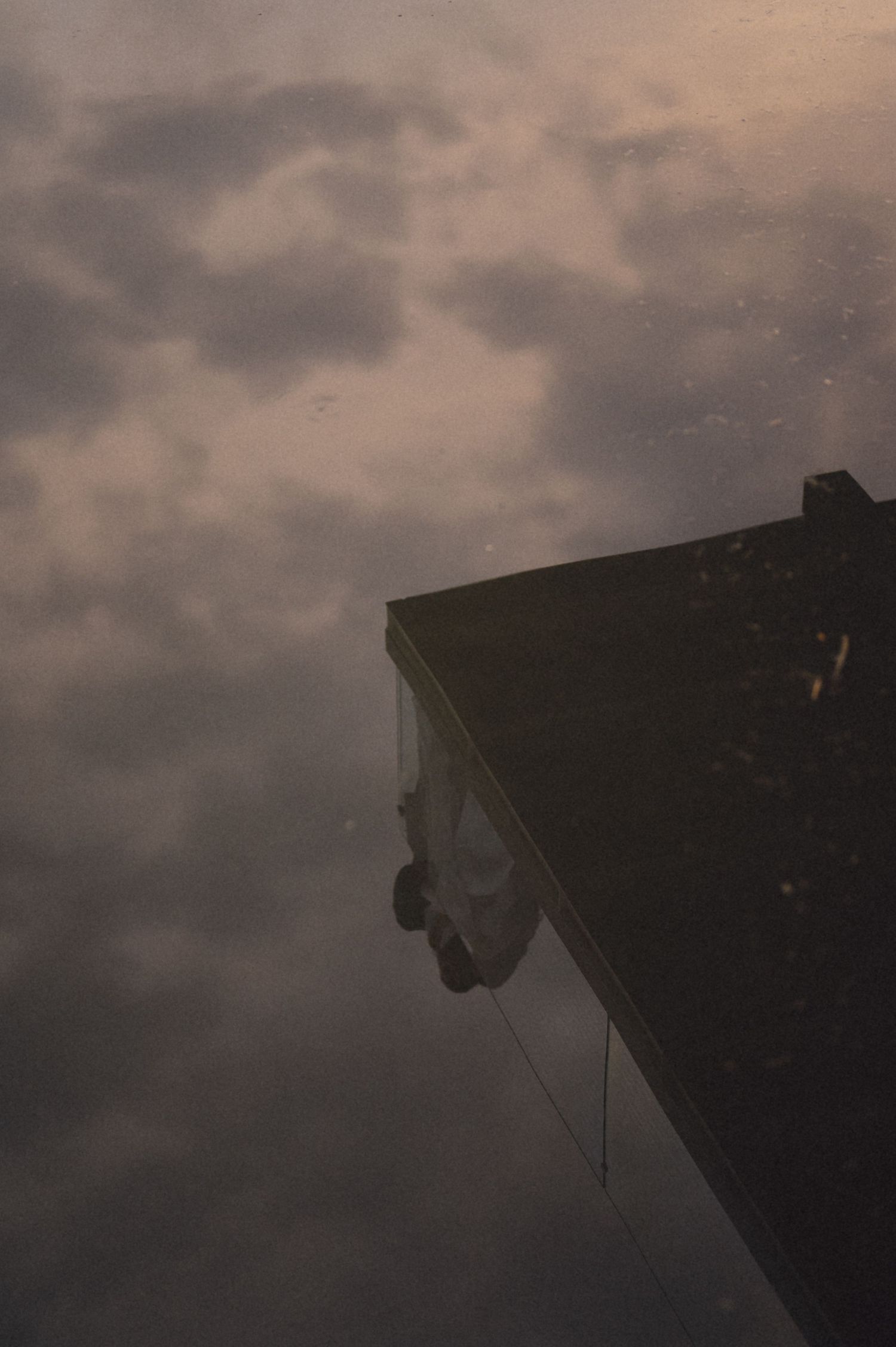 A silhouetted figure hangs precariously from the edge of a dark building against a moody cloudy sky.