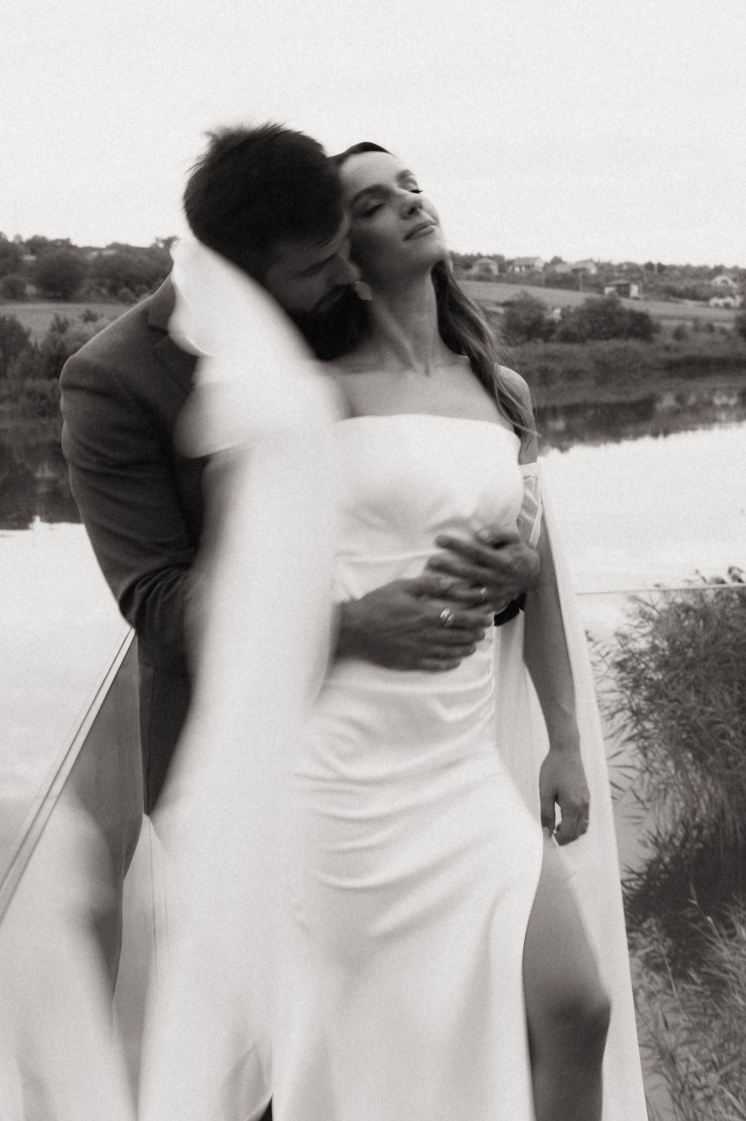 Black and white wedding photos capture intimate embraces between a couple by a scenic waterfront.