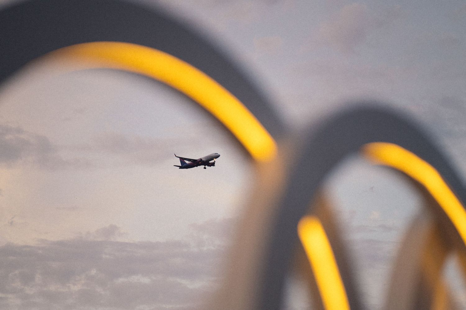 Aircraft silhouette flies through illuminated golden arches at dusk against a cloudy sky background.