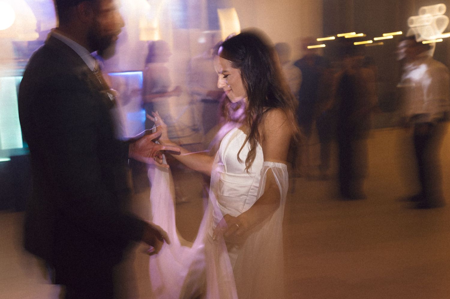 A couple dances together at a dimly lit evening wedding reception with motion blur creating a dreamy atmosphere.