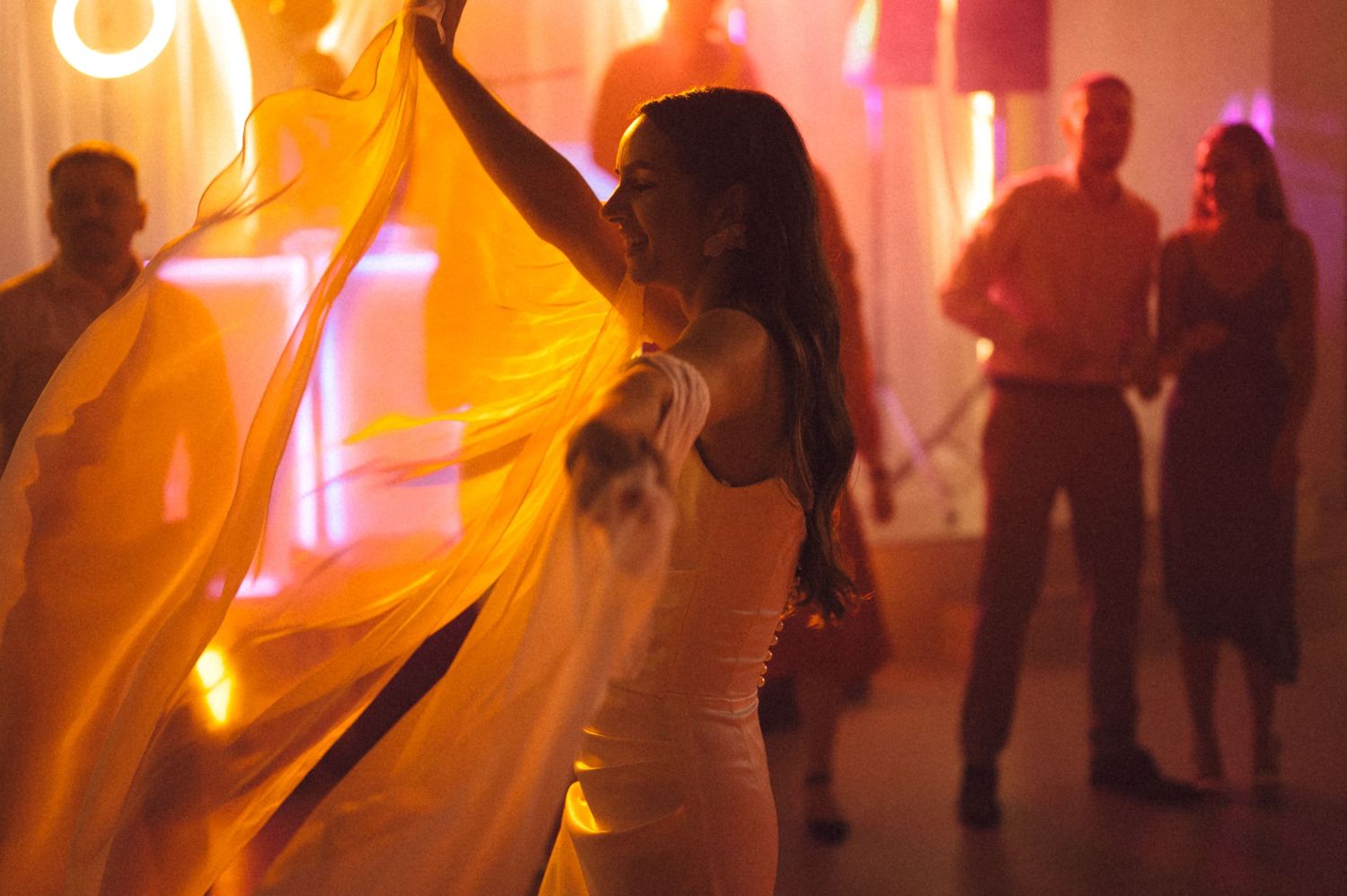 People dancing at a vibrant nightclub with warm orange and pink lighting creating an energetic party atmosphere.