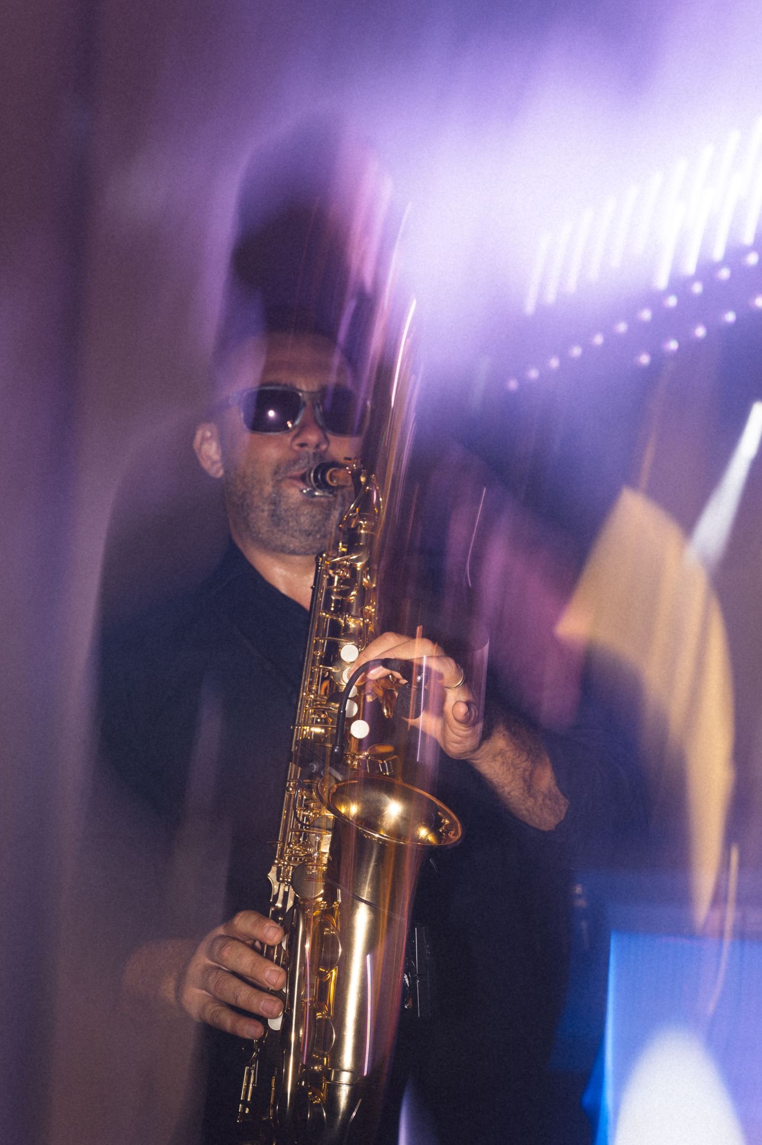 Musician playing saxophone in dramatic purple stage lighting creating an atmospheric silhouette effect.
