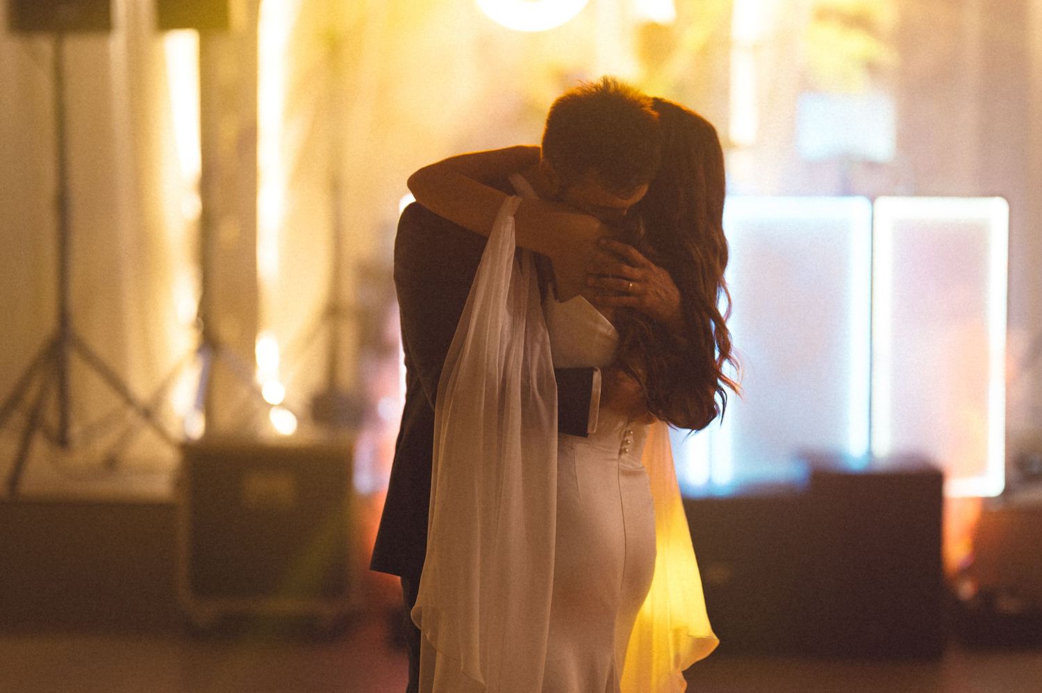 A person in a long white dress stands in front of a window with warm lighting creating a romantic silhouette.