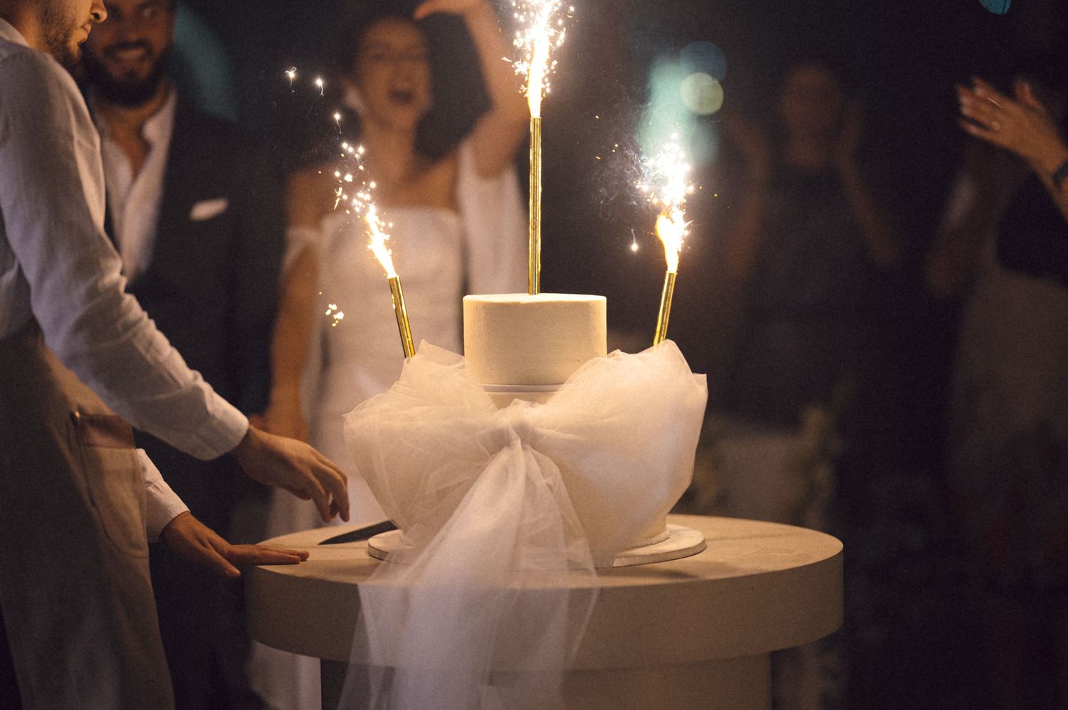 A sequence of sparklers being lit on round tables during a dimly lit evening event.