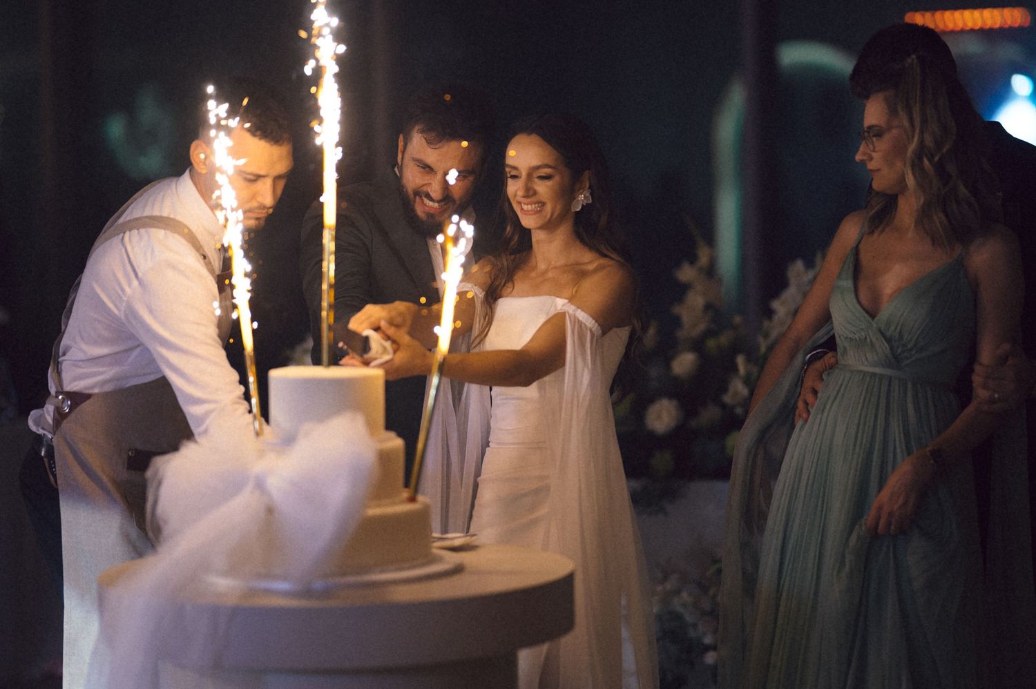 Wedding party members hold sparklers during an evening celebration at an outdoor reception.