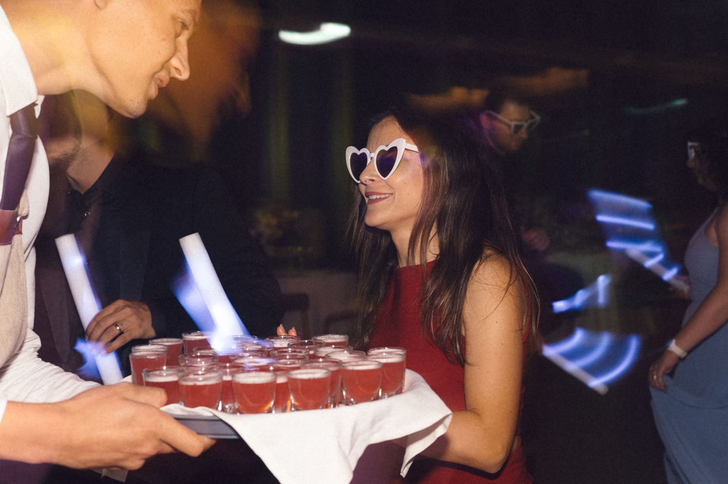 People at a party gather around a table with red cups while socializing in a dimly lit venue.
