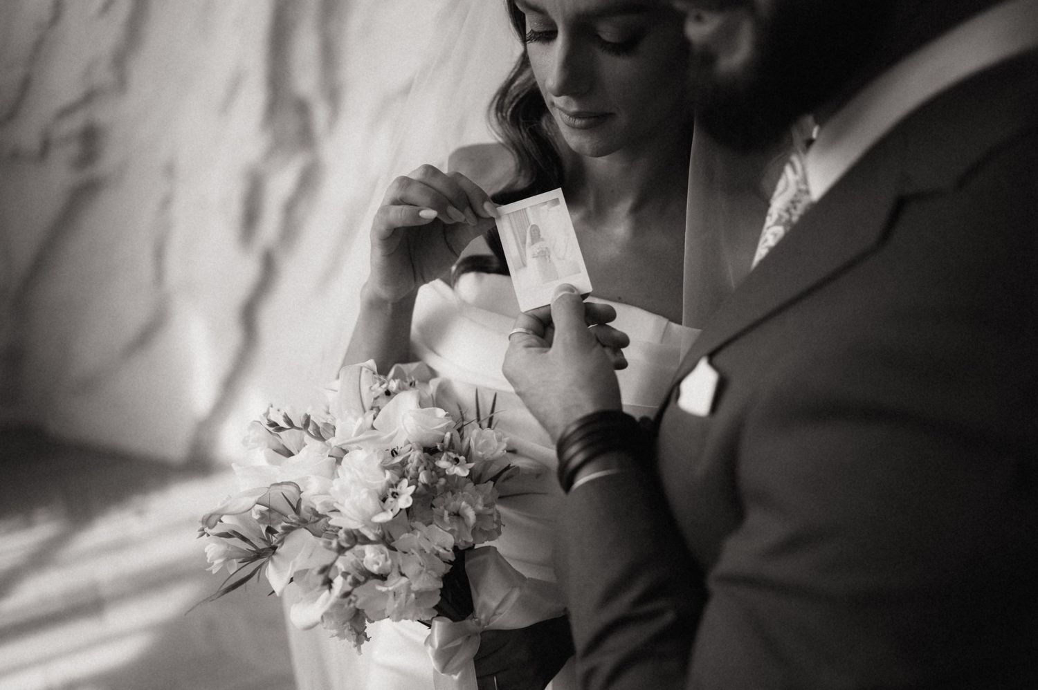 A black and white wedding photograph showing a tender moment with a bouquet of flowers in the foreground.