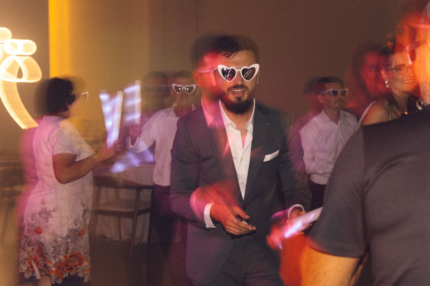 People dancing and socializing at a dimly lit party venue with colorful lighting effects.