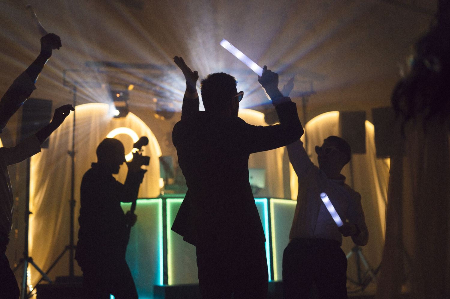 Silhouetted figures dance in front of colorful illuminated walls at a nightclub party.