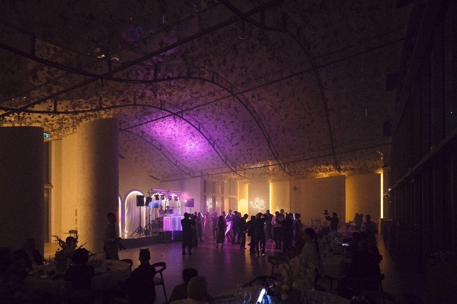 Panoramic view of a dimly lit industrial space with purple lighting and silhouettes of people in the distance.