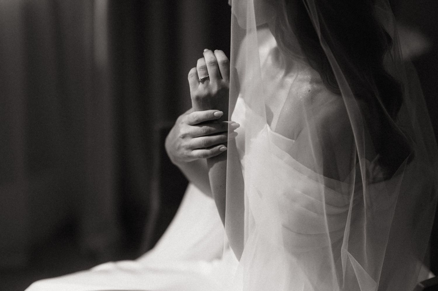 A bride in a white wedding dress and veil holds a bouquet while walking down a dimly lit corridor.