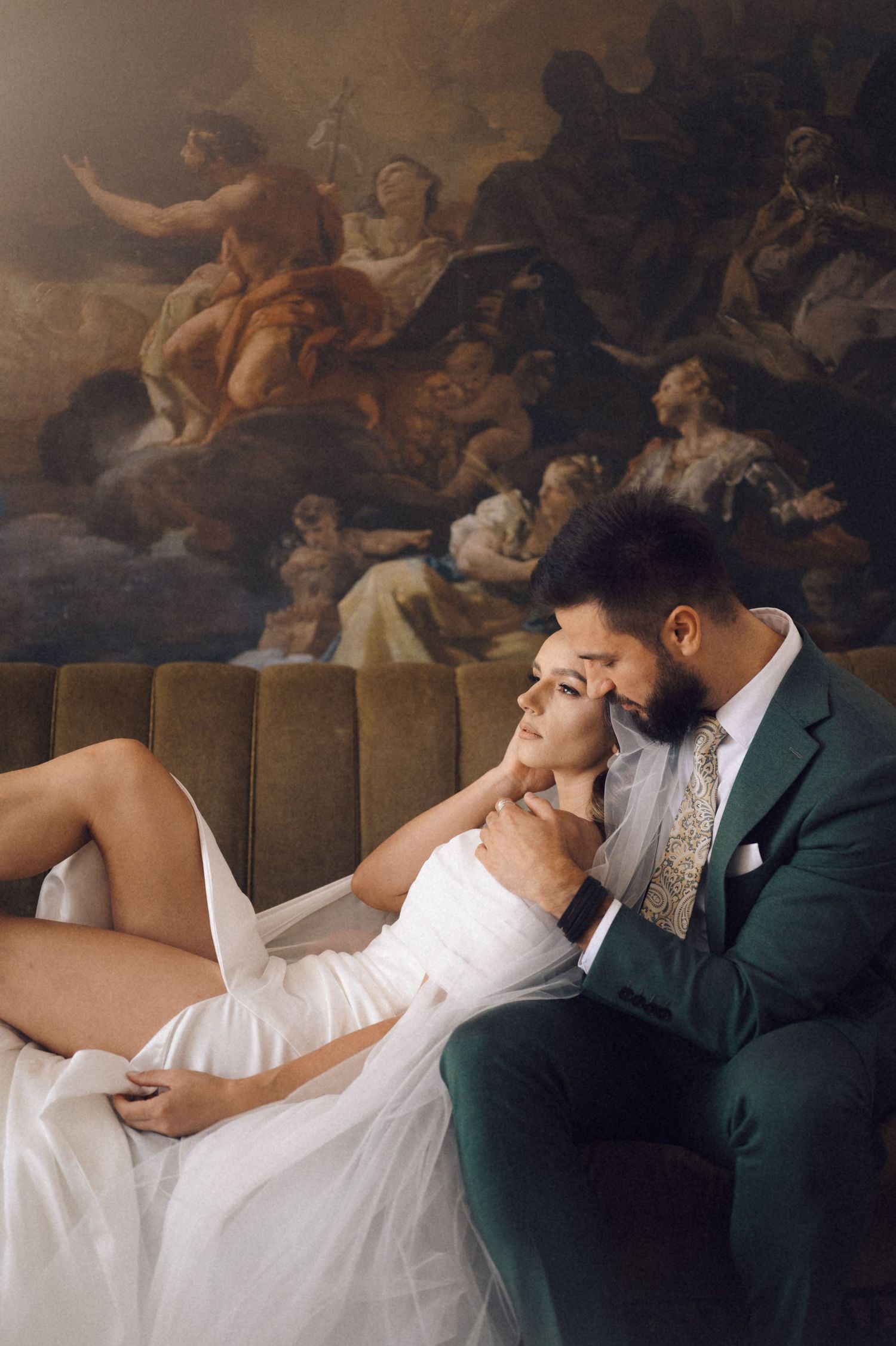 A couple shares a romantic moment on an elegant couch beneath classical artwork on the ceiling.