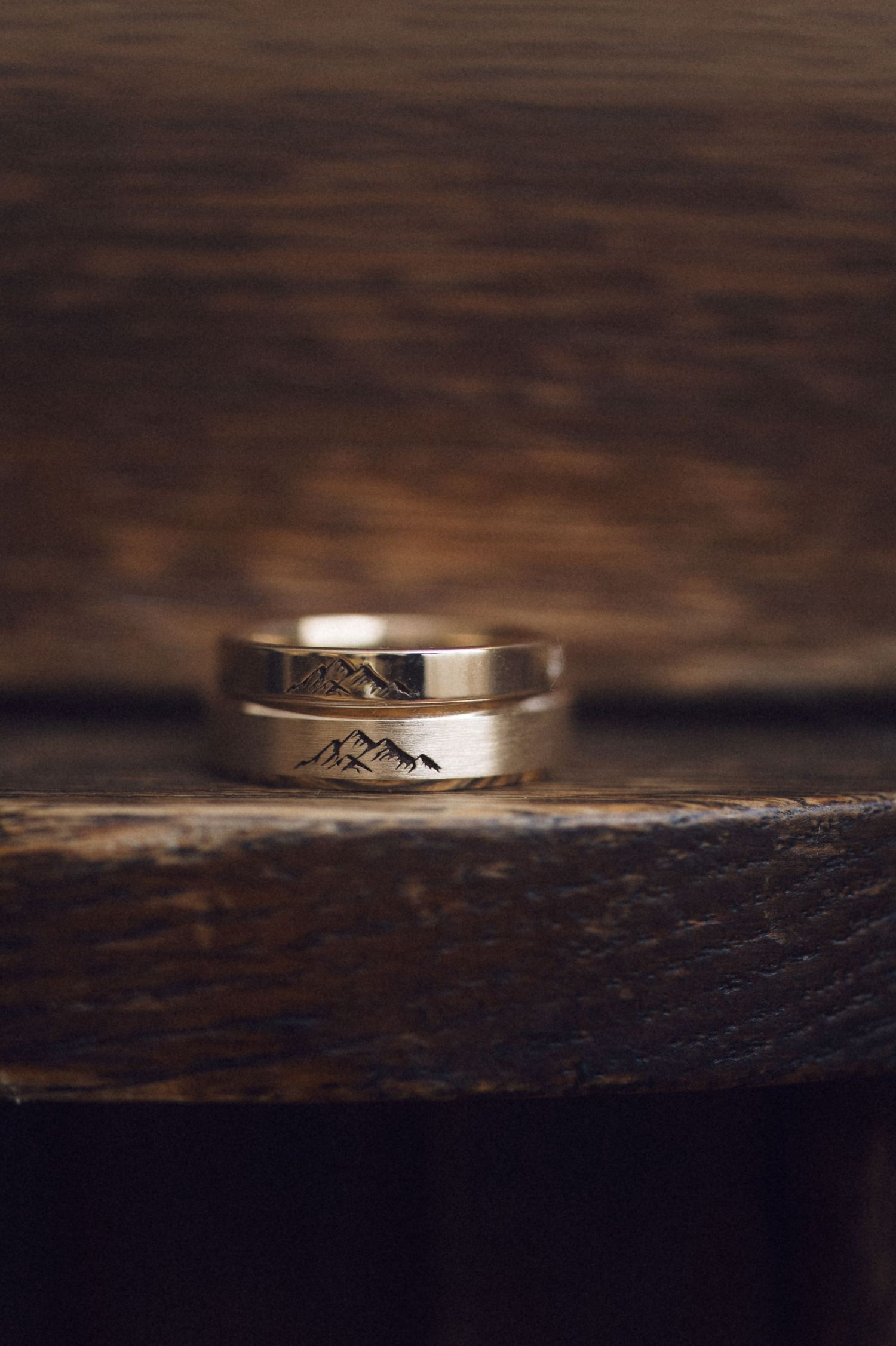 Close-up view of a silver mountain-engraved wedding ring on a dark wooden surface.