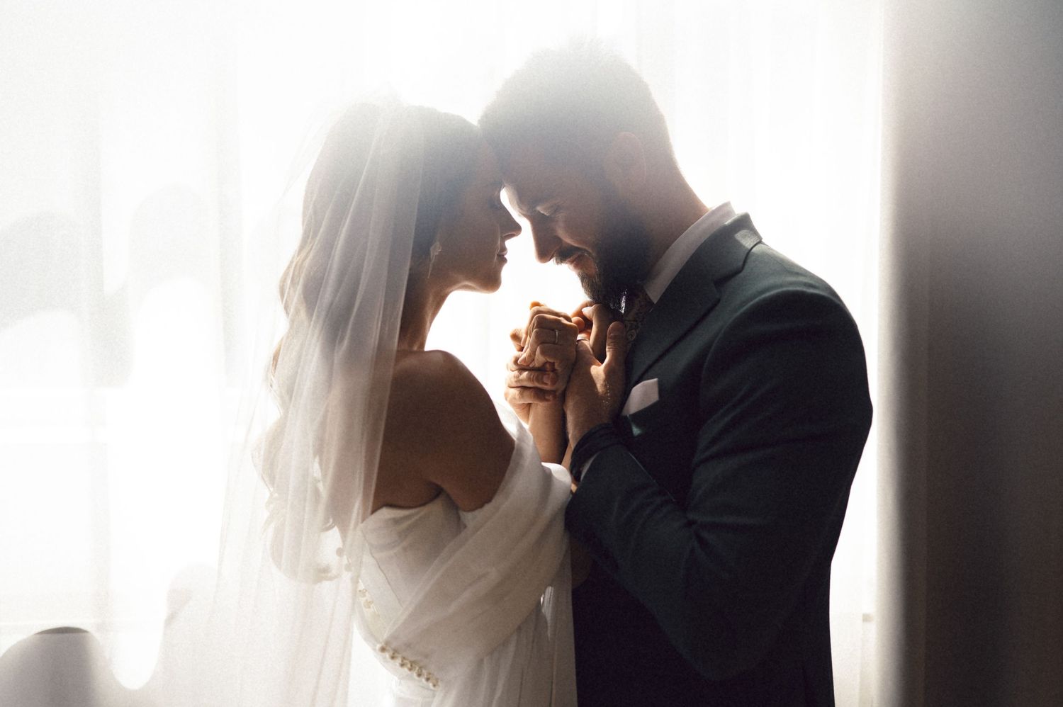 Romantic silhouette of a bride and groom sharing an intimate moment in soft window light.