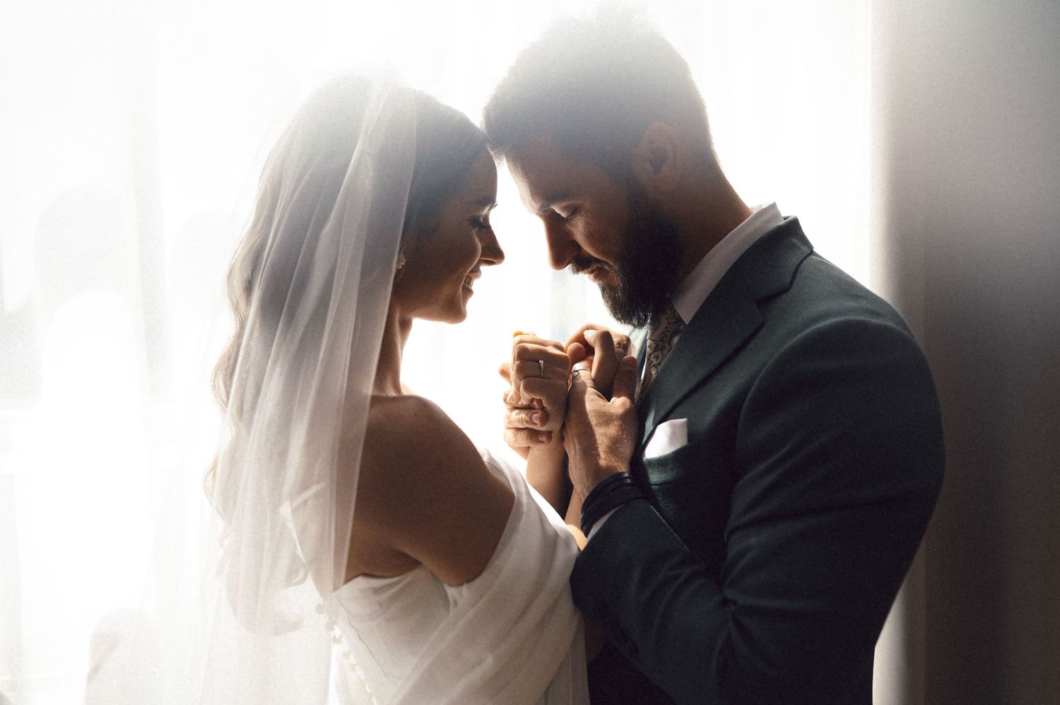 Tender wedding moment captured in silhouette against bright window backlighting.