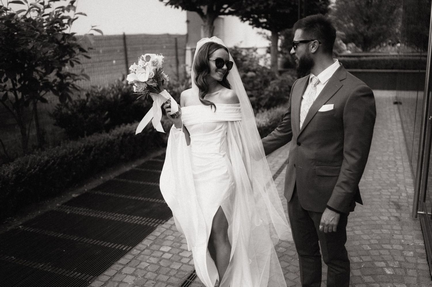 A black and white wedding photo of a couple on a brick path, with the bride in a flowing white dress and veil.